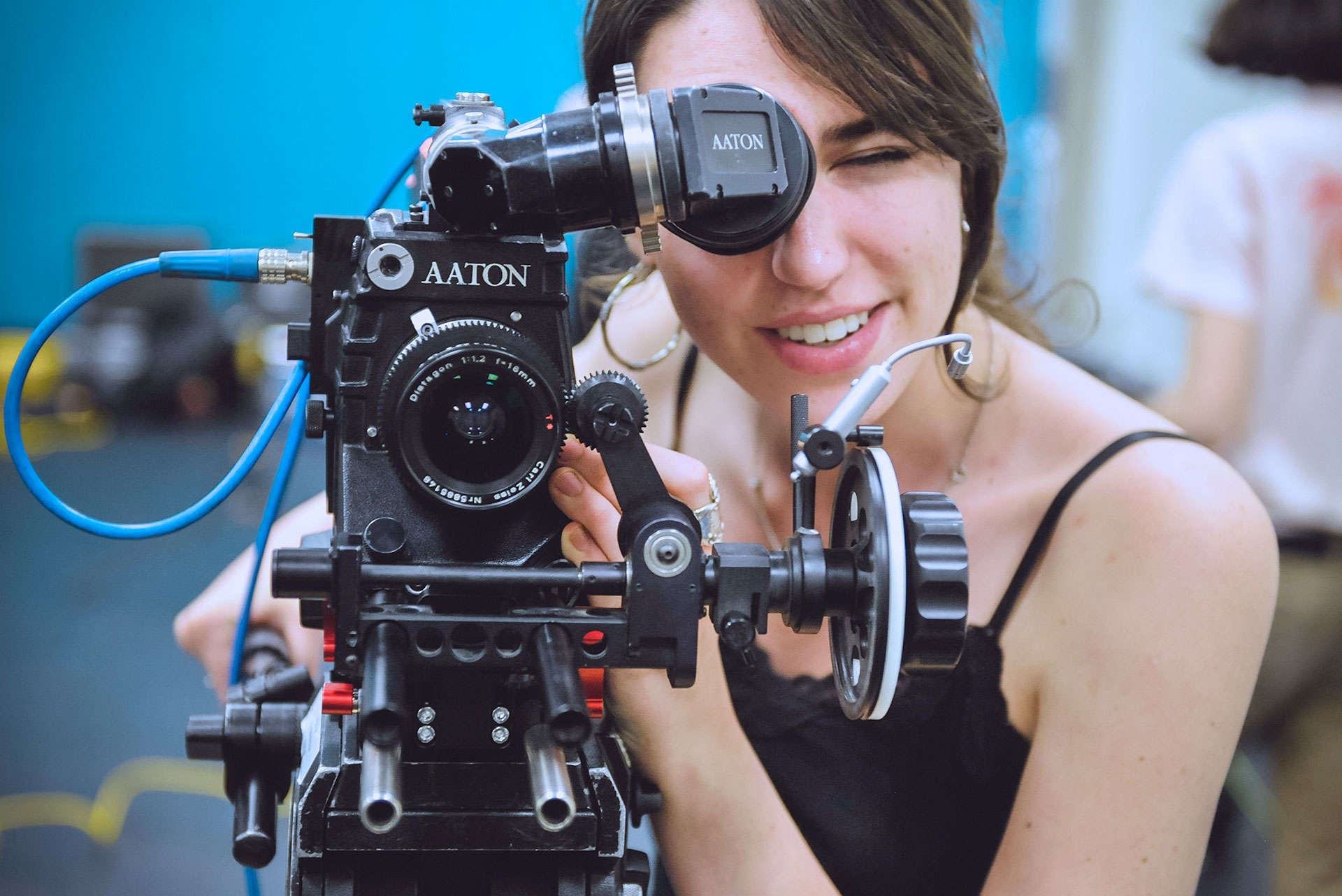 student looking through camera pointed at the viewer with blue background