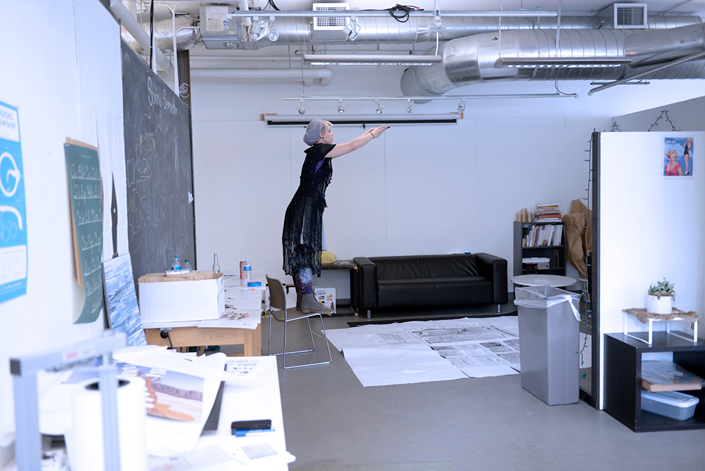 Cornish Design Student standing on a chair in a studio, taking a photo of large scale work on the floor