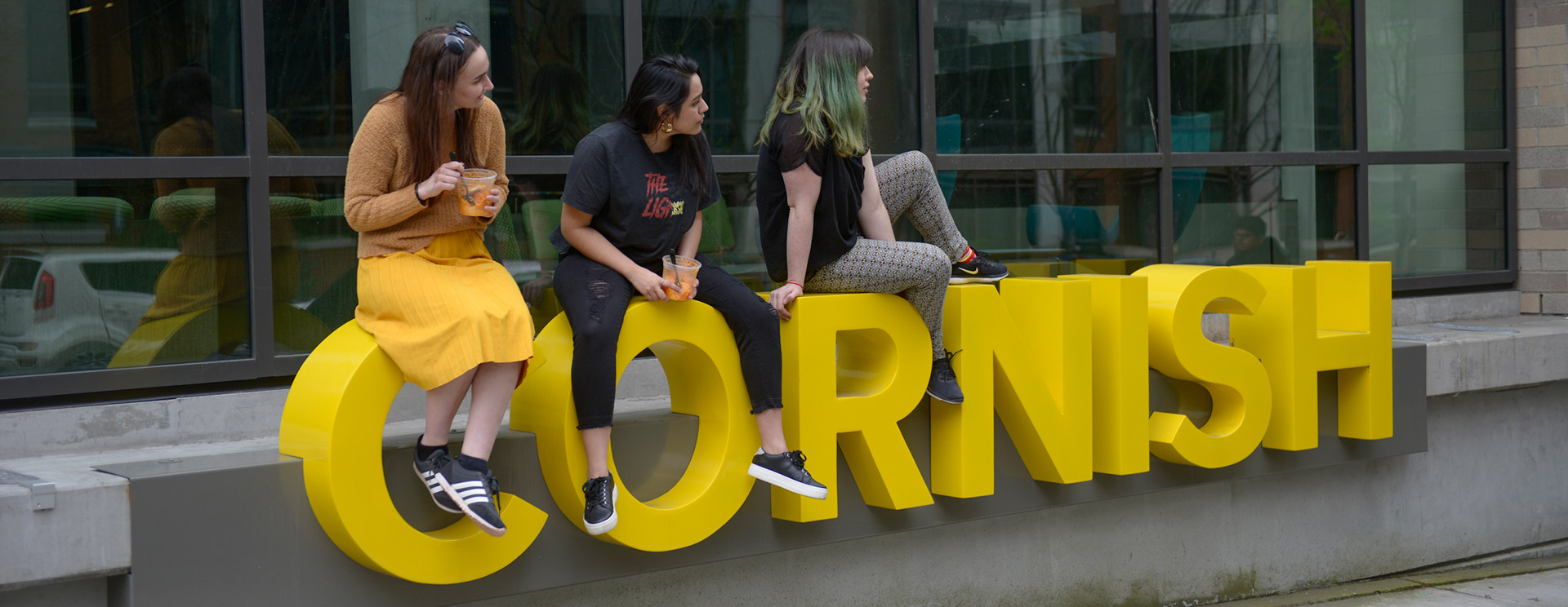 Three Cornish Students at Commons sitting on letters that spell 