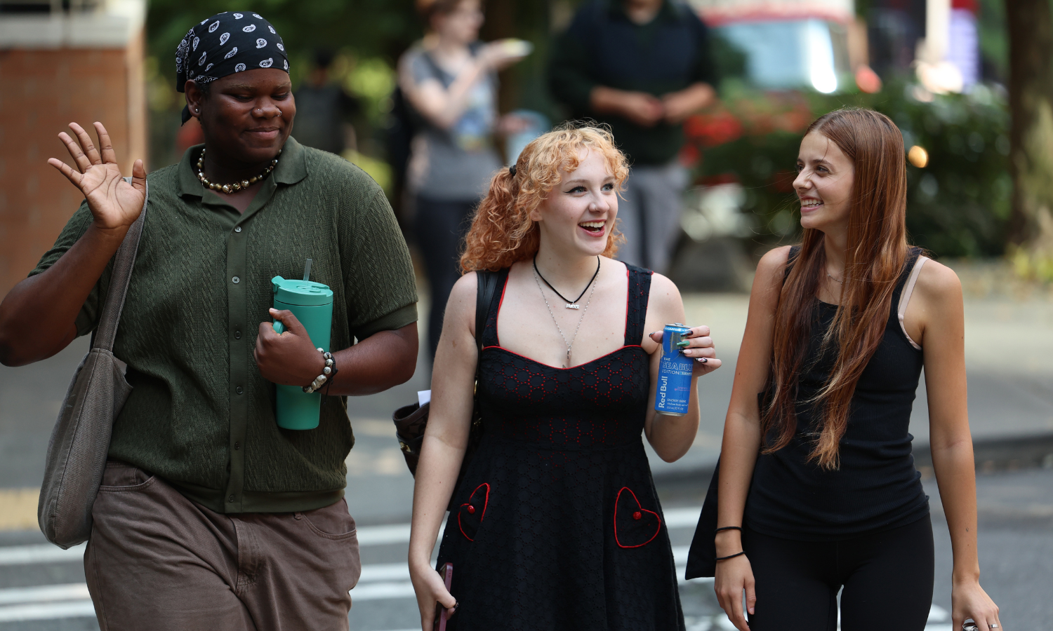 Photo of three students crossing the street and waiving at the camera