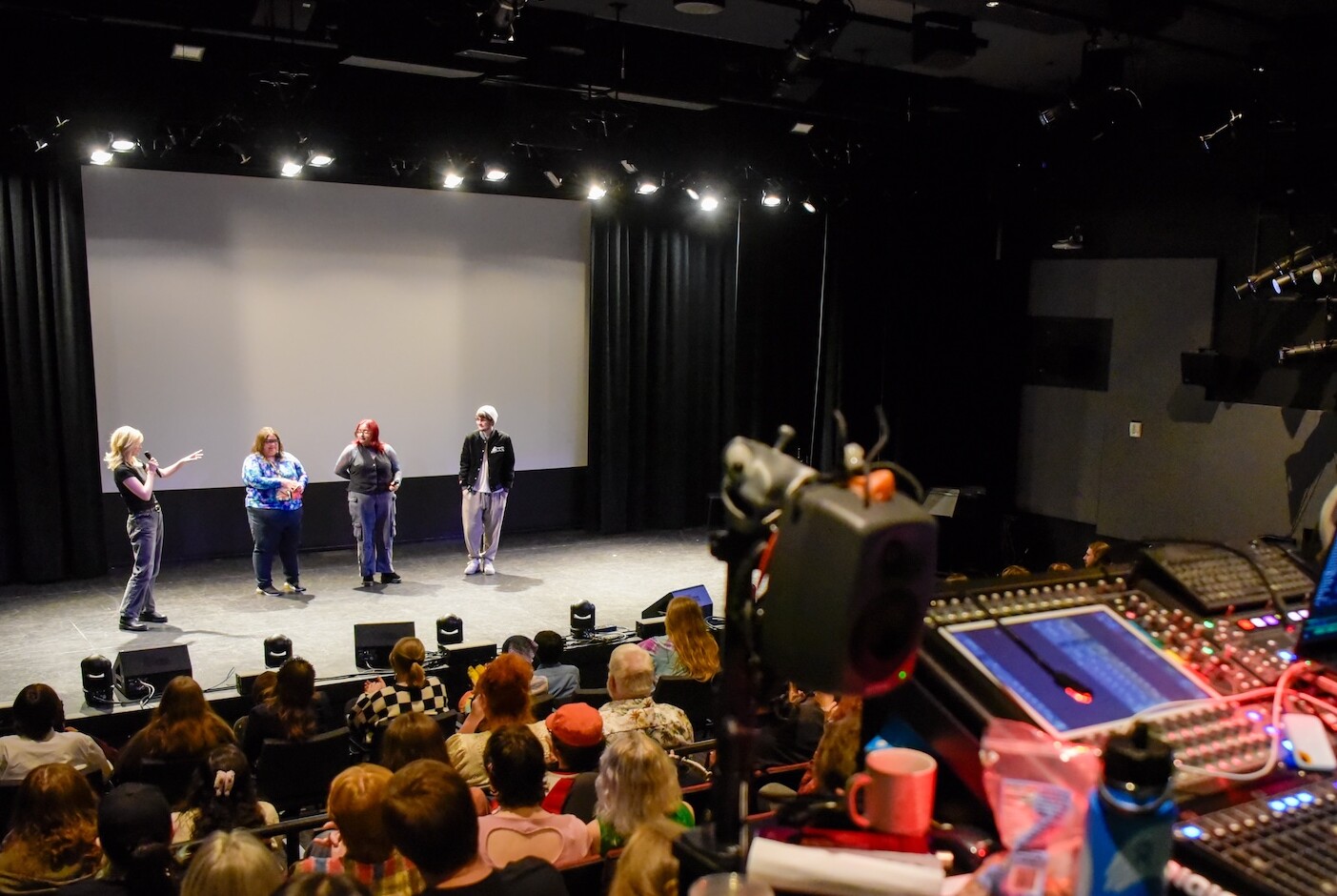 Wide angle shot of Raisbeck Audiorium with a few people on stage and a full crowd.