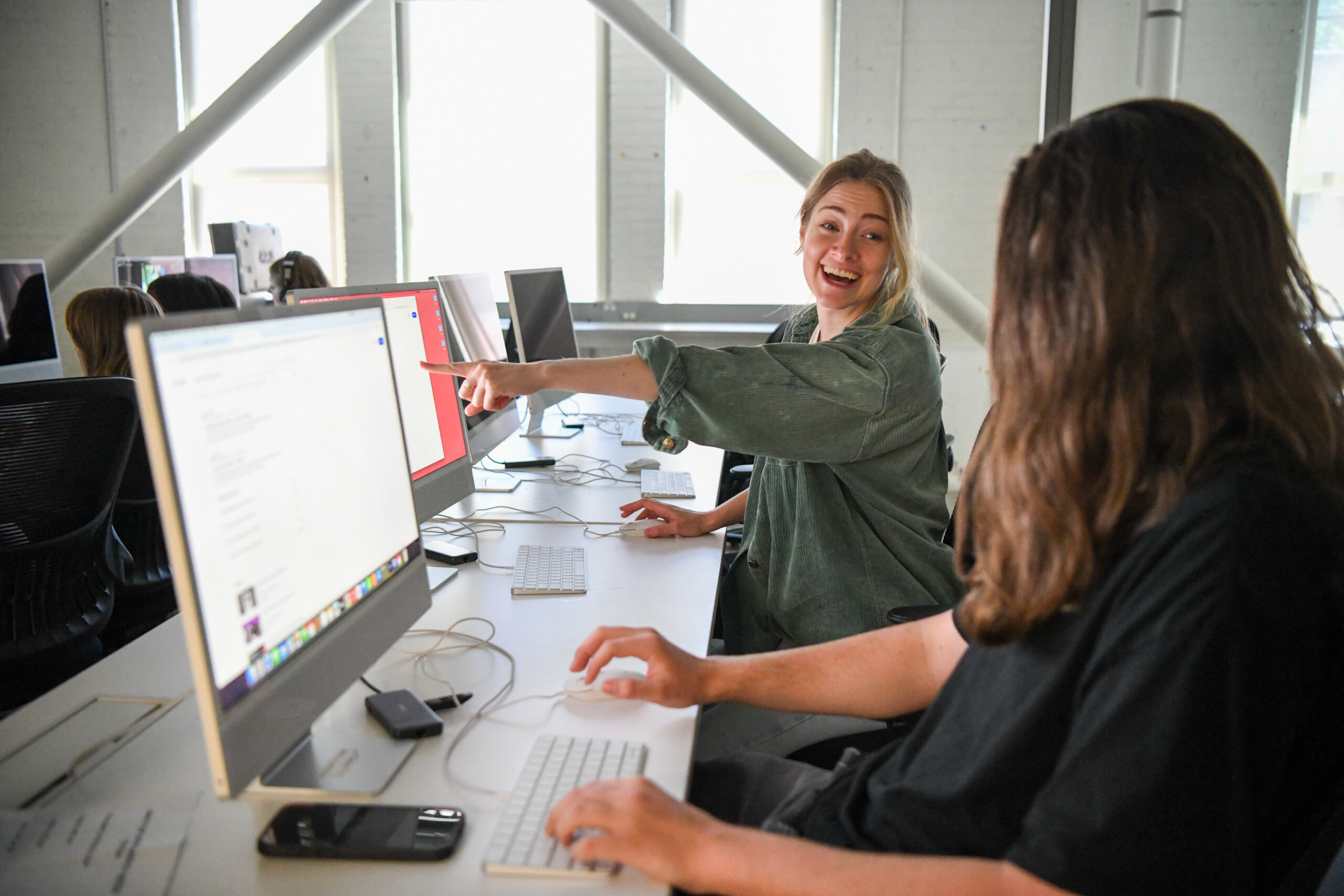 Young woman at a computer in the Cornish computer lab pointing at a screen in excitement to another student.